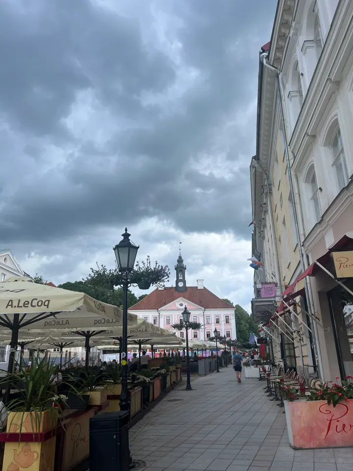 Tartu's town hall across Raekoja plats, café umbrellas in the foreground under a storm sky